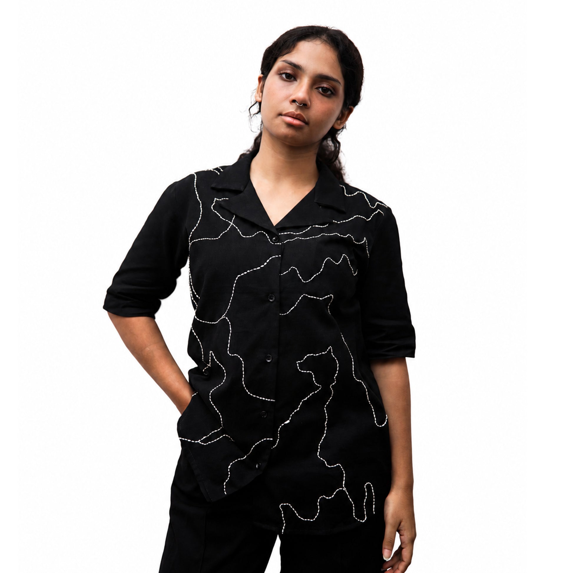 A woman modeling a black short-sleeve button-up shirt with white abstract line patterns, set against a plain white background.