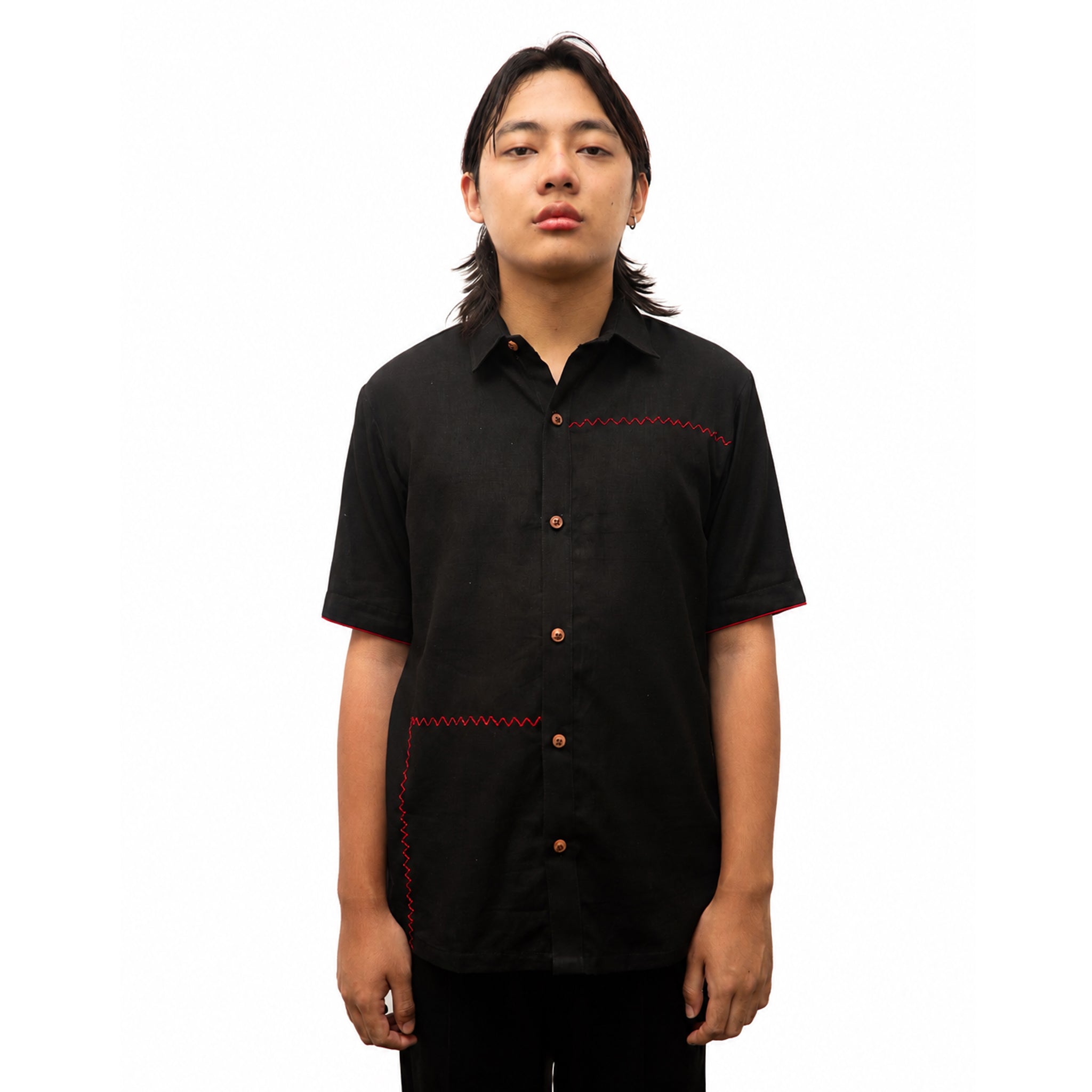 A man wearing a black short-sleeve button-up shirt with red contrast stitching details on the chest and pocket, photographed against a solid white background.